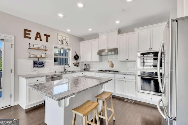 kitchen with stainless steel appliances, white cabinetry, sink, and light stone counters