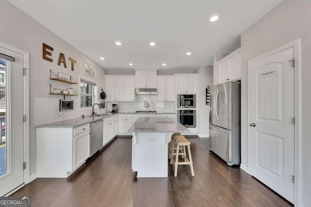 kitchen featuring a breakfast bar, stainless steel appliances, a center island, light stone counters, and white cabinets