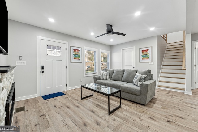 living room featuring a stone fireplace, light hardwood / wood-style floors, and ceiling fan