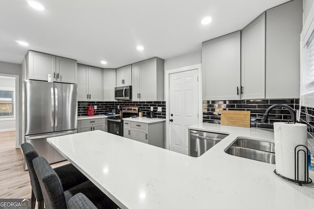 kitchen with sink, light hardwood / wood-style flooring, gray cabinetry, backsplash, and stainless steel appliances