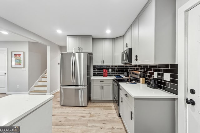 kitchen with stainless steel appliances, tasteful backsplash, gray cabinets, and light hardwood / wood-style flooring