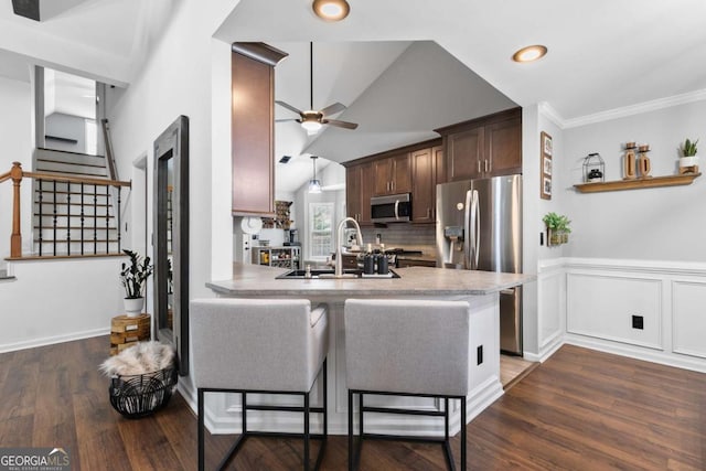 kitchen featuring appliances with stainless steel finishes, kitchen peninsula, a kitchen bar, dark brown cabinetry, and ceiling fan