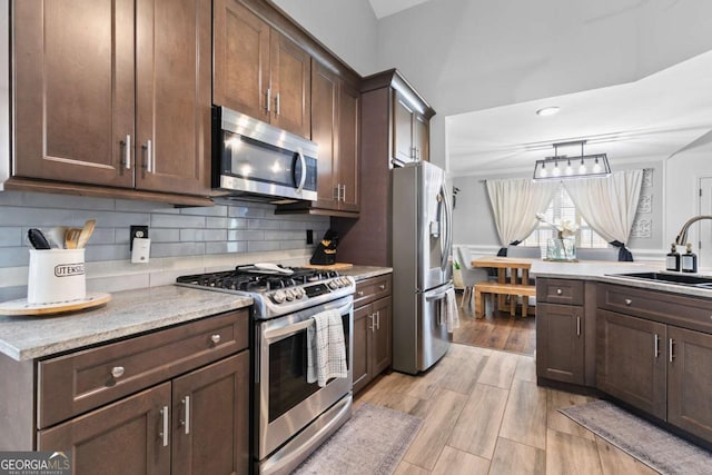 kitchen with dark brown cabinetry, appliances with stainless steel finishes, light hardwood / wood-style floors, and sink