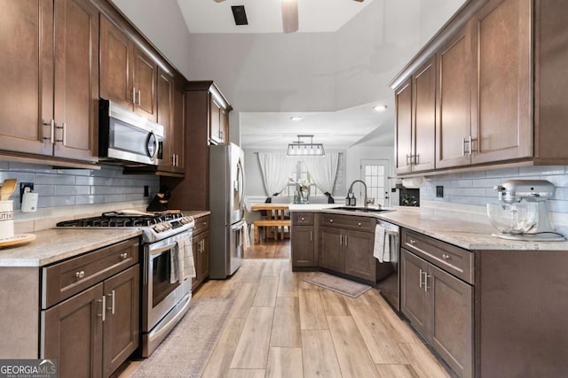 kitchen with sink, light hardwood / wood-style flooring, kitchen peninsula, stainless steel appliances, and backsplash