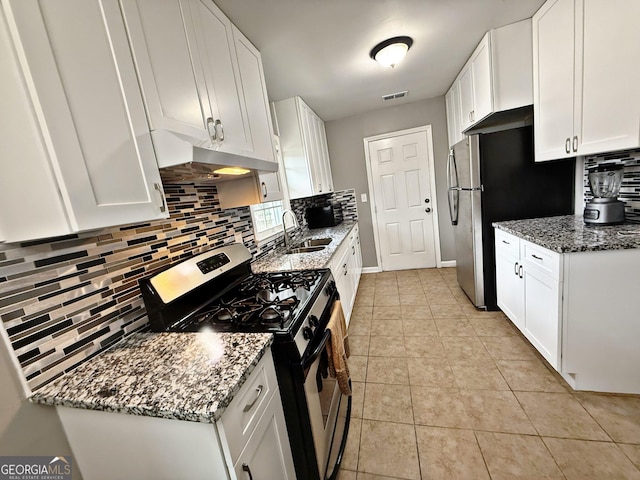 kitchen with appliances with stainless steel finishes, light tile patterned floors, white cabinetry, dark stone counters, and decorative backsplash