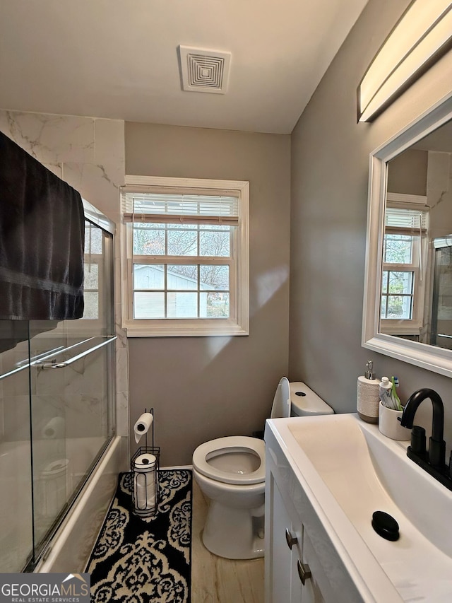 full bathroom with enclosed tub / shower combo, vanity, and toilet