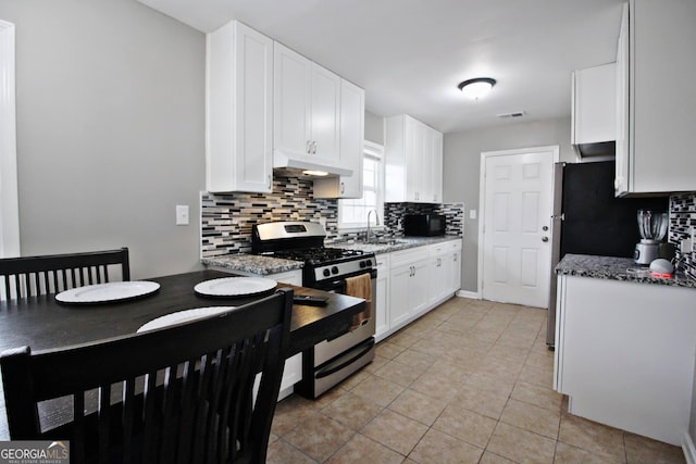 kitchen with white cabinetry, stainless steel range with gas stovetop, light stone countertops, sink, and backsplash