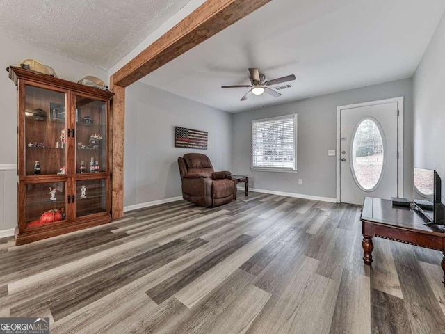 living area with beamed ceiling, ceiling fan, a textured ceiling, and dark hardwood / wood-style flooring