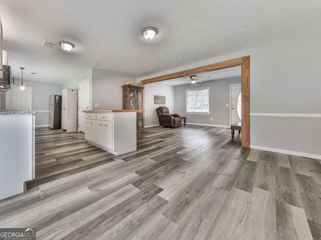 kitchen with white cabinetry, wood-type flooring, a textured ceiling, stainless steel fridge, and pendant lighting