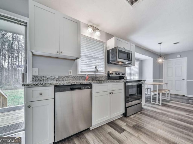 kitchen featuring sink, light hardwood / wood-style flooring, appliances with stainless steel finishes, hanging light fixtures, and white cabinets