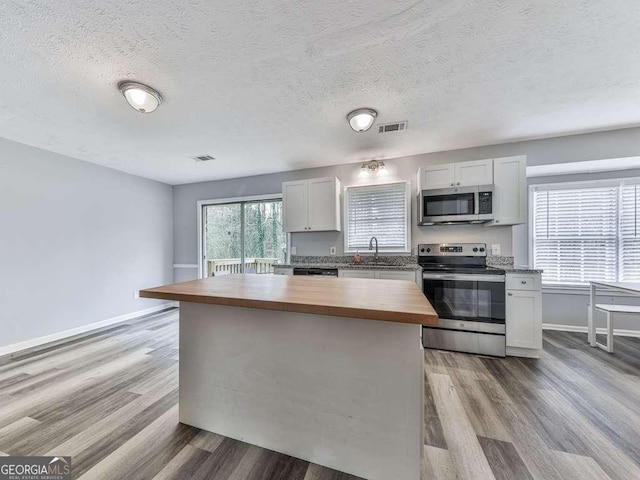 kitchen featuring stainless steel appliances, butcher block counters, a kitchen island, and white cabinets