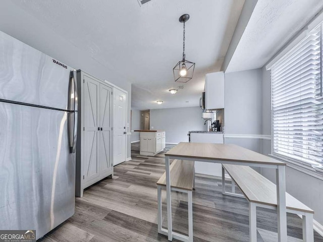 kitchen with stainless steel appliances, white cabinets, light hardwood / wood-style floors, and decorative light fixtures