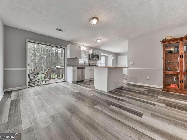 kitchen with decorative light fixtures, a center island, stainless steel appliances, hardwood / wood-style floors, and white cabinets