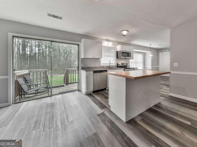 kitchen with appliances with stainless steel finishes, pendant lighting, butcher block counters, white cabinets, and dark wood-type flooring