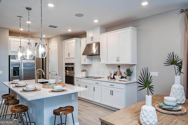 kitchen with a breakfast bar area, white cabinetry, pendant lighting, stainless steel appliances, and a kitchen island with sink