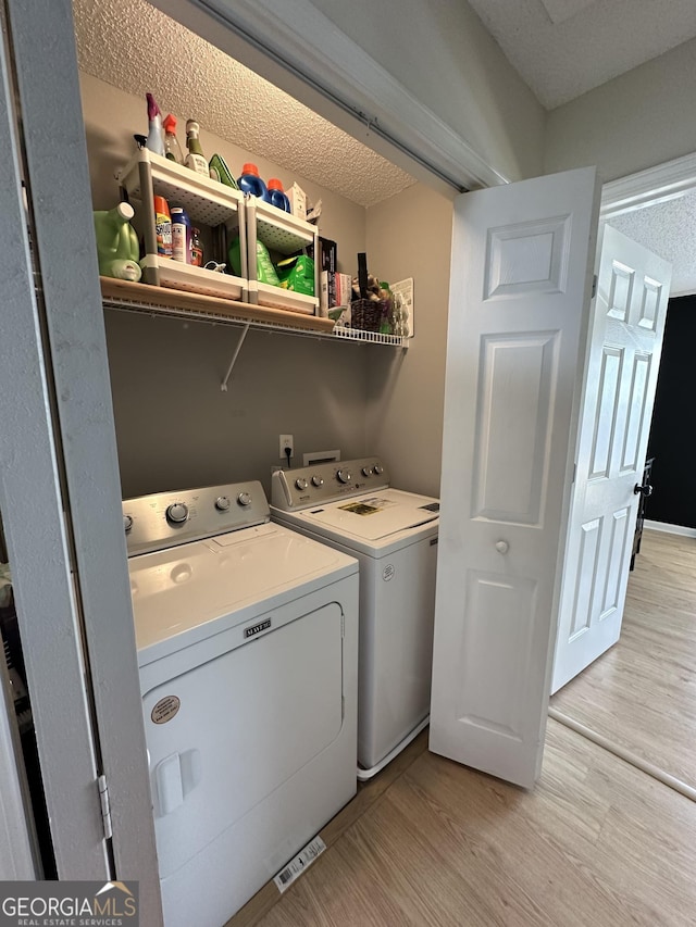 laundry area with independent washer and dryer, a textured ceiling, and light wood-type flooring