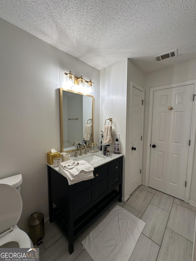 bathroom featuring vanity, a textured ceiling, and toilet