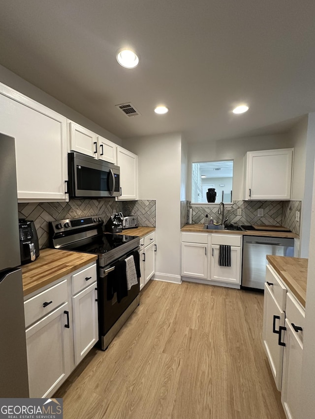 kitchen with white cabinetry, wood counters, stainless steel appliances, and light wood-type flooring