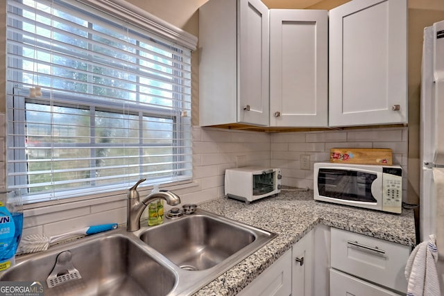 kitchen featuring a healthy amount of sunlight, sink, tasteful backsplash, and white cabinets