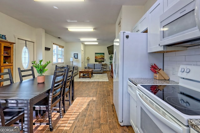 kitchen with white cabinetry, decorative backsplash, light stone counters, dark wood-type flooring, and white appliances