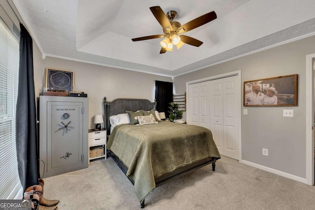 carpeted bedroom featuring ceiling fan, a tray ceiling, ornamental molding, a textured ceiling, and a closet