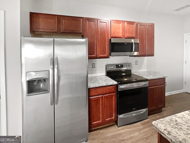 kitchen featuring light stone counters, appliances with stainless steel finishes, tasteful backsplash, and light hardwood / wood-style flooring