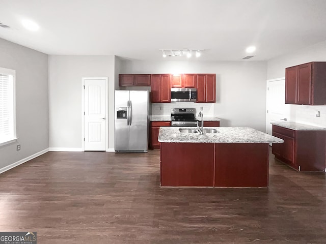 kitchen featuring appliances with stainless steel finishes, sink, dark hardwood / wood-style flooring, light stone counters, and a center island with sink