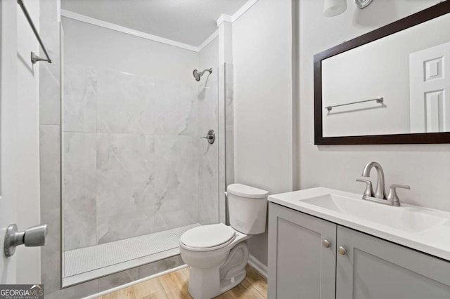 bathroom featuring crown molding, hardwood / wood-style flooring, vanity, a tile shower, and toilet