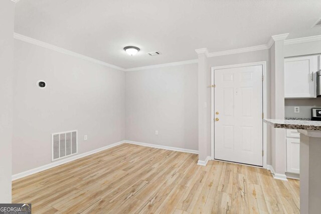 interior space with ornamental molding, light stone counters, white cabinets, and light hardwood / wood-style floors