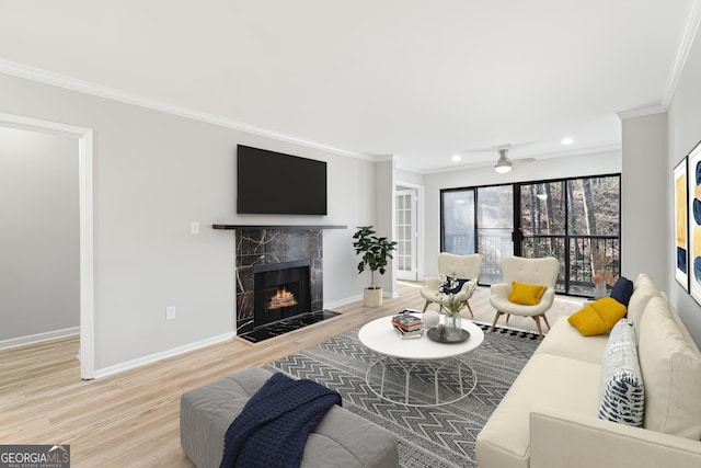 living room featuring ceiling fan, ornamental molding, a premium fireplace, and wood-type flooring