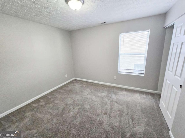 empty room with dark carpet and a textured ceiling