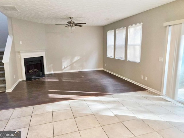 unfurnished living room featuring light tile patterned flooring, a textured ceiling, and ceiling fan