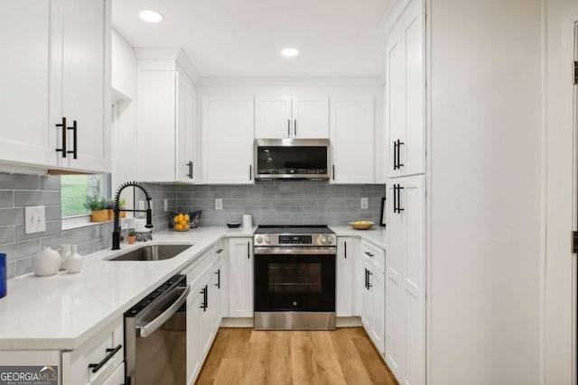 kitchen with sink, appliances with stainless steel finishes, white cabinetry, tasteful backsplash, and light hardwood / wood-style floors