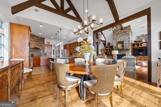 dining area featuring beam ceiling, a stone fireplace, light hardwood / wood-style flooring, and high vaulted ceiling