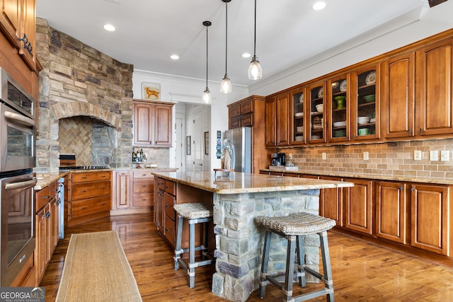 kitchen with appliances with stainless steel finishes, decorative light fixtures, a kitchen bar, a center island, and light stone countertops