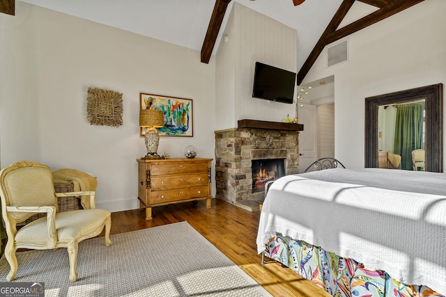 bedroom with hardwood / wood-style flooring, a stone fireplace, high vaulted ceiling, and beamed ceiling