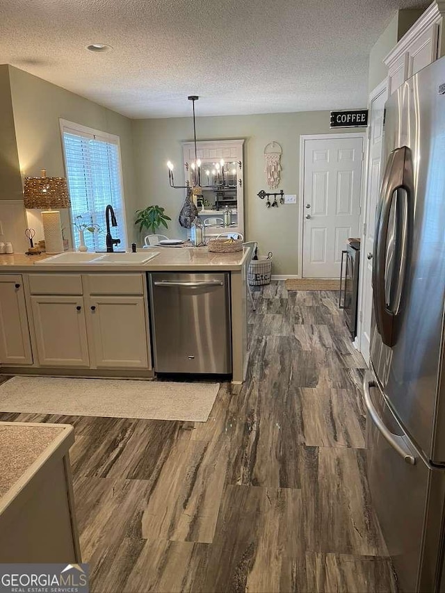 kitchen with pendant lighting, sink, dark hardwood / wood-style flooring, stainless steel appliances, and a textured ceiling