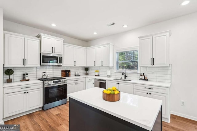 kitchen with appliances with stainless steel finishes, light hardwood / wood-style floors, sink, and white cabinets