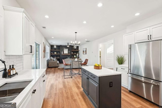 kitchen with stainless steel fridge, white cabinetry, light hardwood / wood-style floors, a kitchen island, and decorative light fixtures