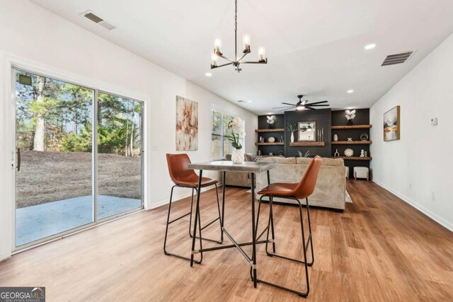 dining space with ceiling fan with notable chandelier and light hardwood / wood-style floors