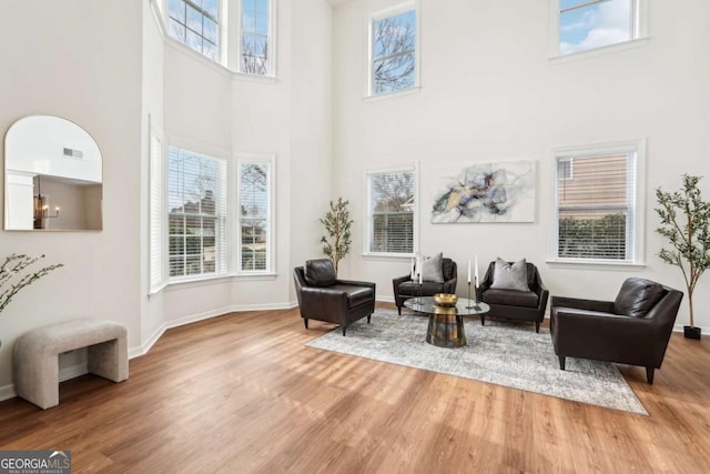 living area with a healthy amount of sunlight, hardwood / wood-style floors, and a towering ceiling