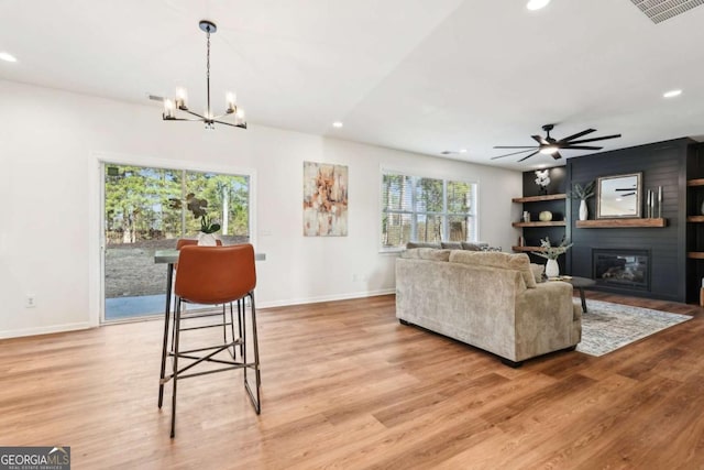 living room with ceiling fan with notable chandelier, light hardwood / wood-style floors, and a large fireplace