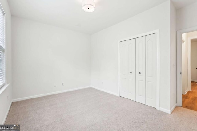 unfurnished bedroom with multiple windows, light colored carpet, and a closet