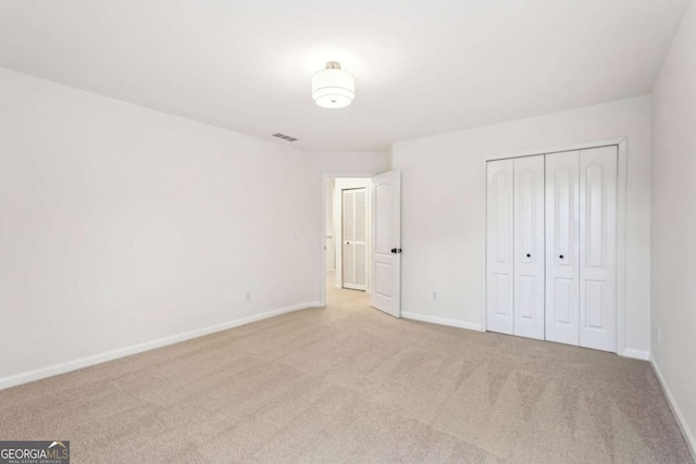 unfurnished bedroom with light colored carpet and a closet