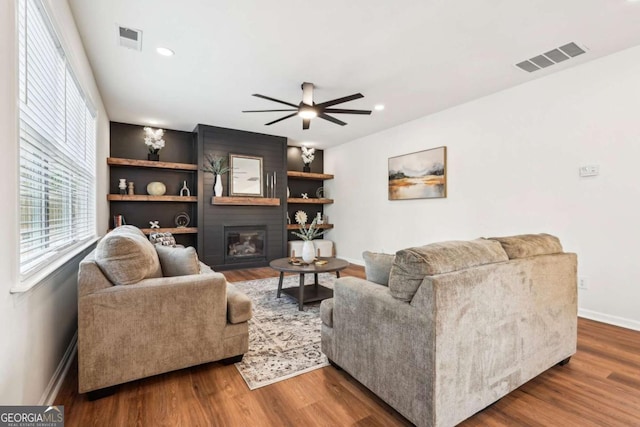 living room with wood-type flooring, a large fireplace, and ceiling fan