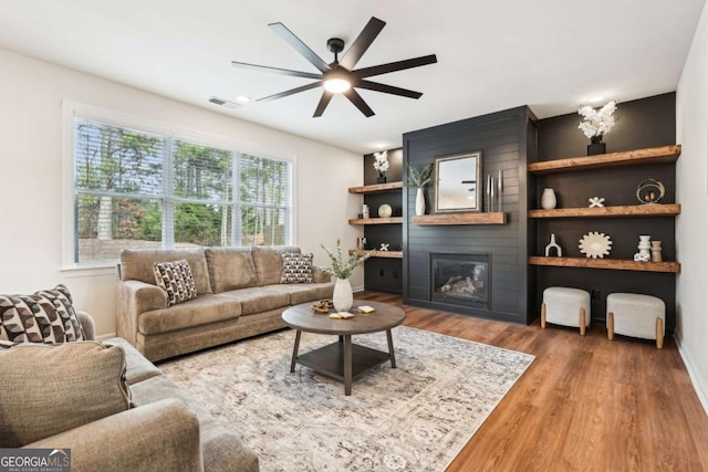 living room with wood-type flooring, a large fireplace, and ceiling fan