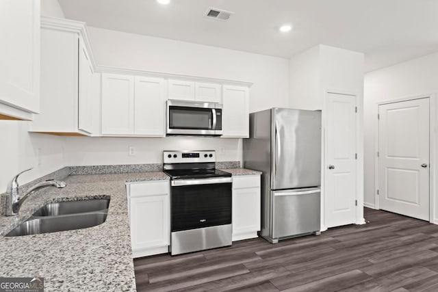 kitchen featuring appliances with stainless steel finishes, sink, white cabinets, dark hardwood / wood-style flooring, and light stone countertops