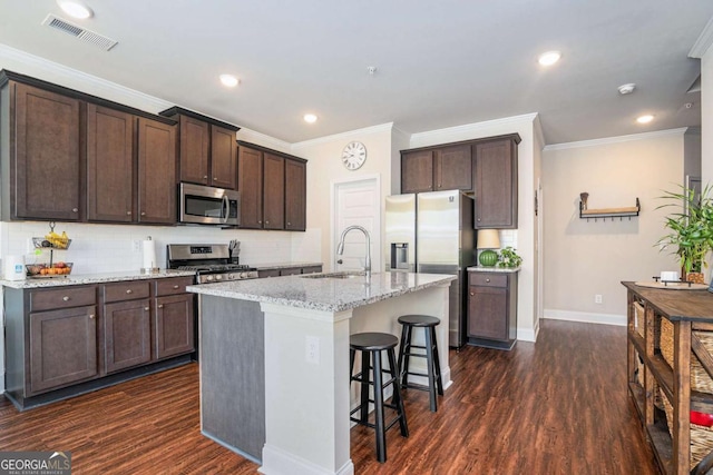 kitchen with sink, stainless steel appliances, dark hardwood / wood-style floors, light stone counters, and an island with sink