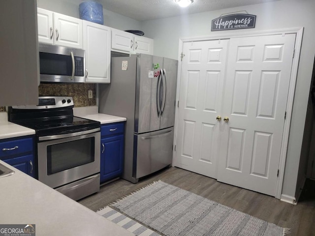 kitchen with dark wood-type flooring, blue cabinetry, appliances with stainless steel finishes, white cabinets, and decorative backsplash