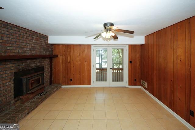 unfurnished living room with light tile patterned flooring, french doors, ceiling fan, and wood walls